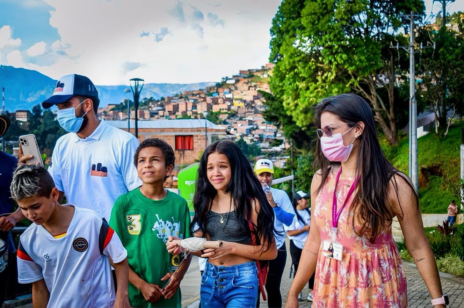 Children and a volunteer walking through a hillside barrio in Medellín, with brick houses on the mountainside behind them